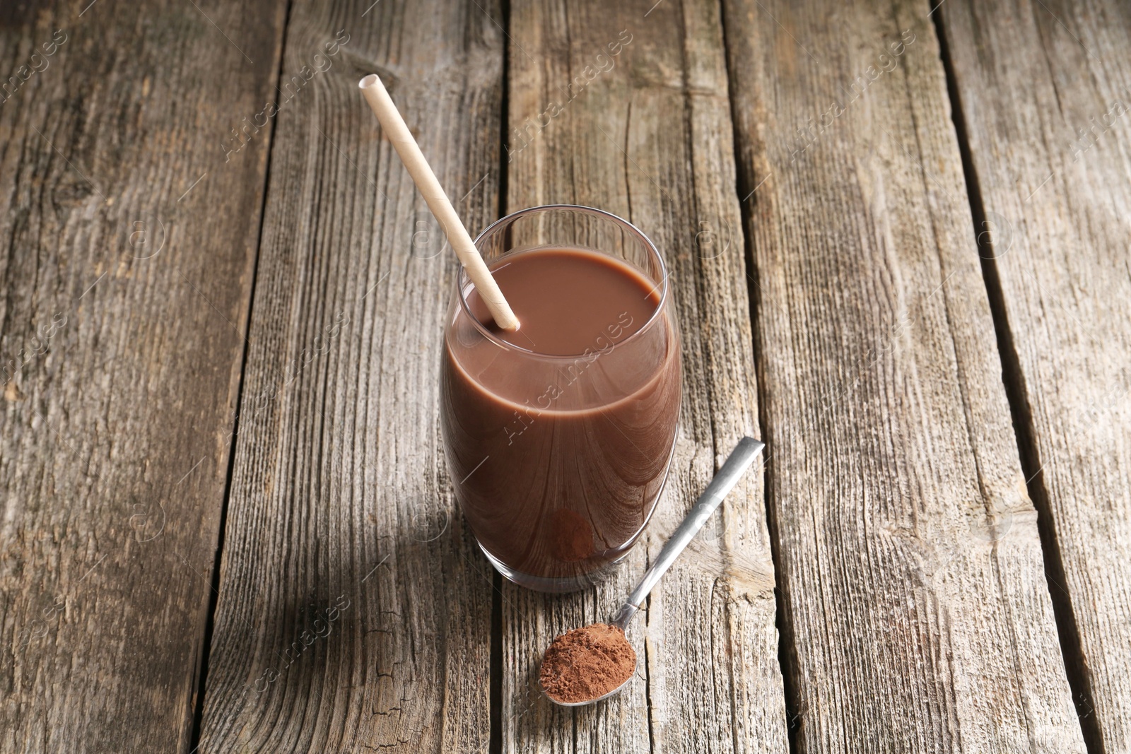 Photo of Delicious protein shake in glass and spoon with powder on wooden table