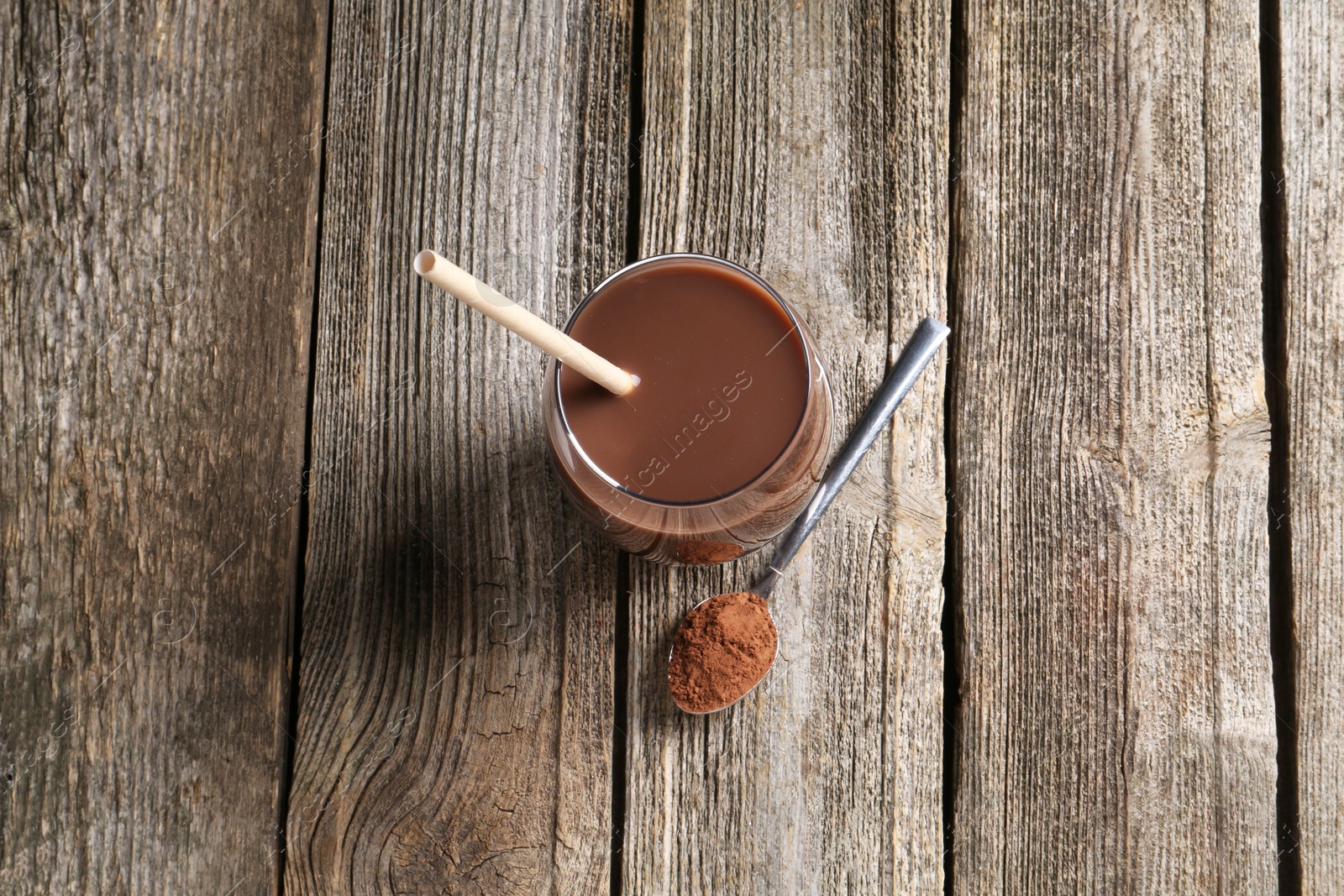 Photo of Delicious protein shake in glass and spoon with powder on wooden table, top view