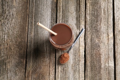 Photo of Delicious protein shake in glass and spoon with powder on wooden table, top view