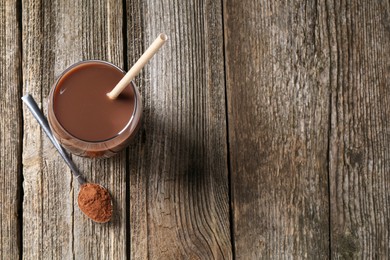 Photo of Delicious protein shake in glass and spoon with powder on wooden table, top view. Space for text