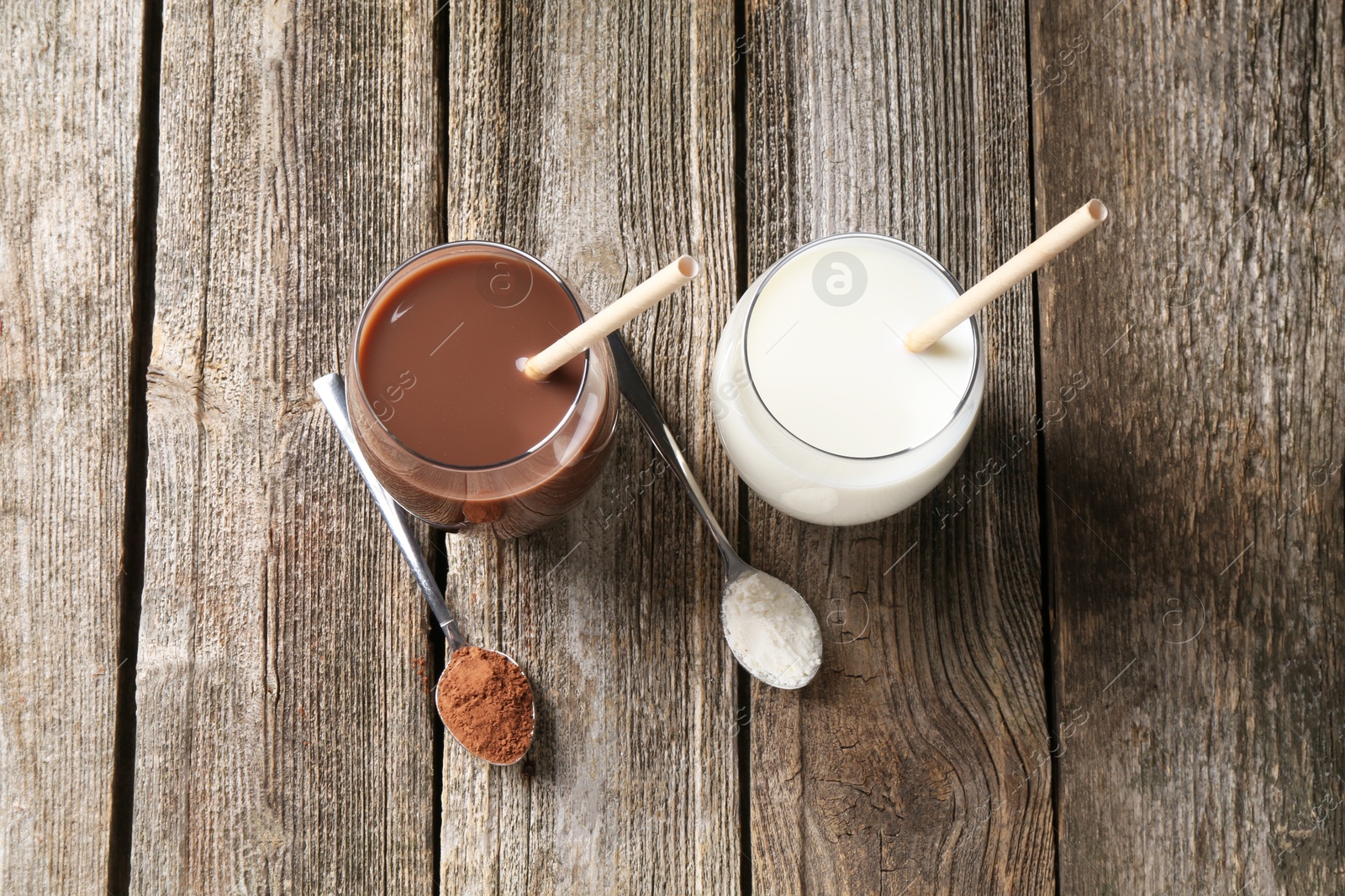 Photo of Delicious protein shakes in glasses and spoons with powder on wooden table, flat lay