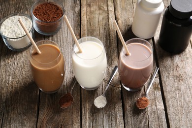 Photo of Delicious protein shakes in glasses, powder, spoons and plastic bottles on wooden table