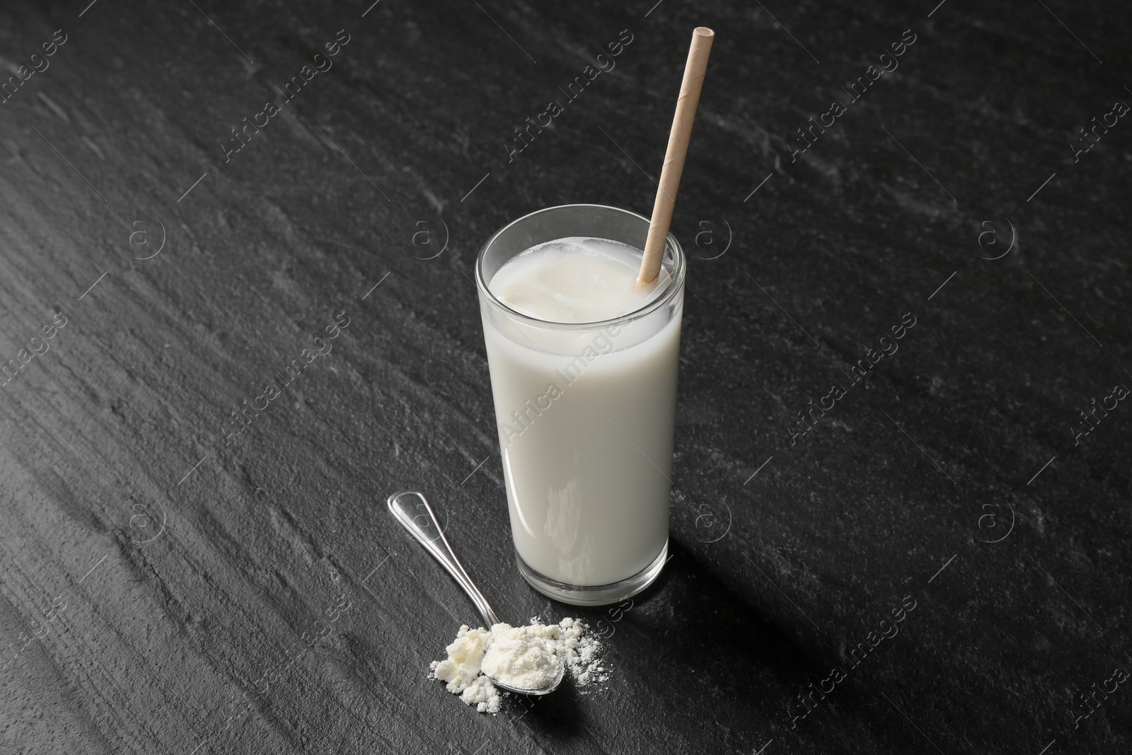 Photo of Delicious protein shake in glass and spoon with powder on black table