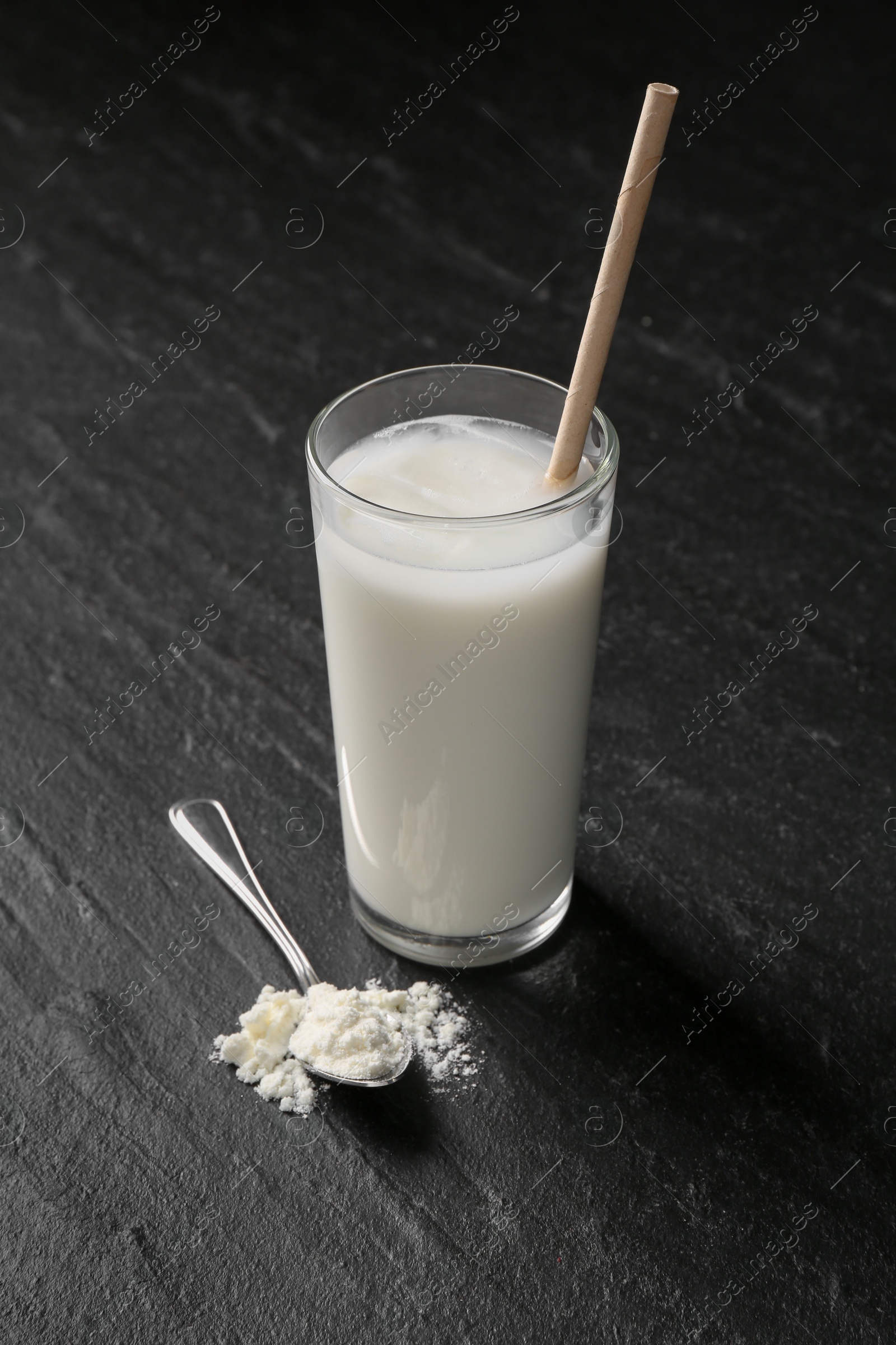 Photo of Delicious protein shake in glass and spoon with powder on black table