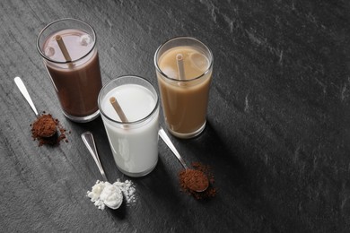 Delicious protein shakes in glasses and spoons with powder on black table, space for text