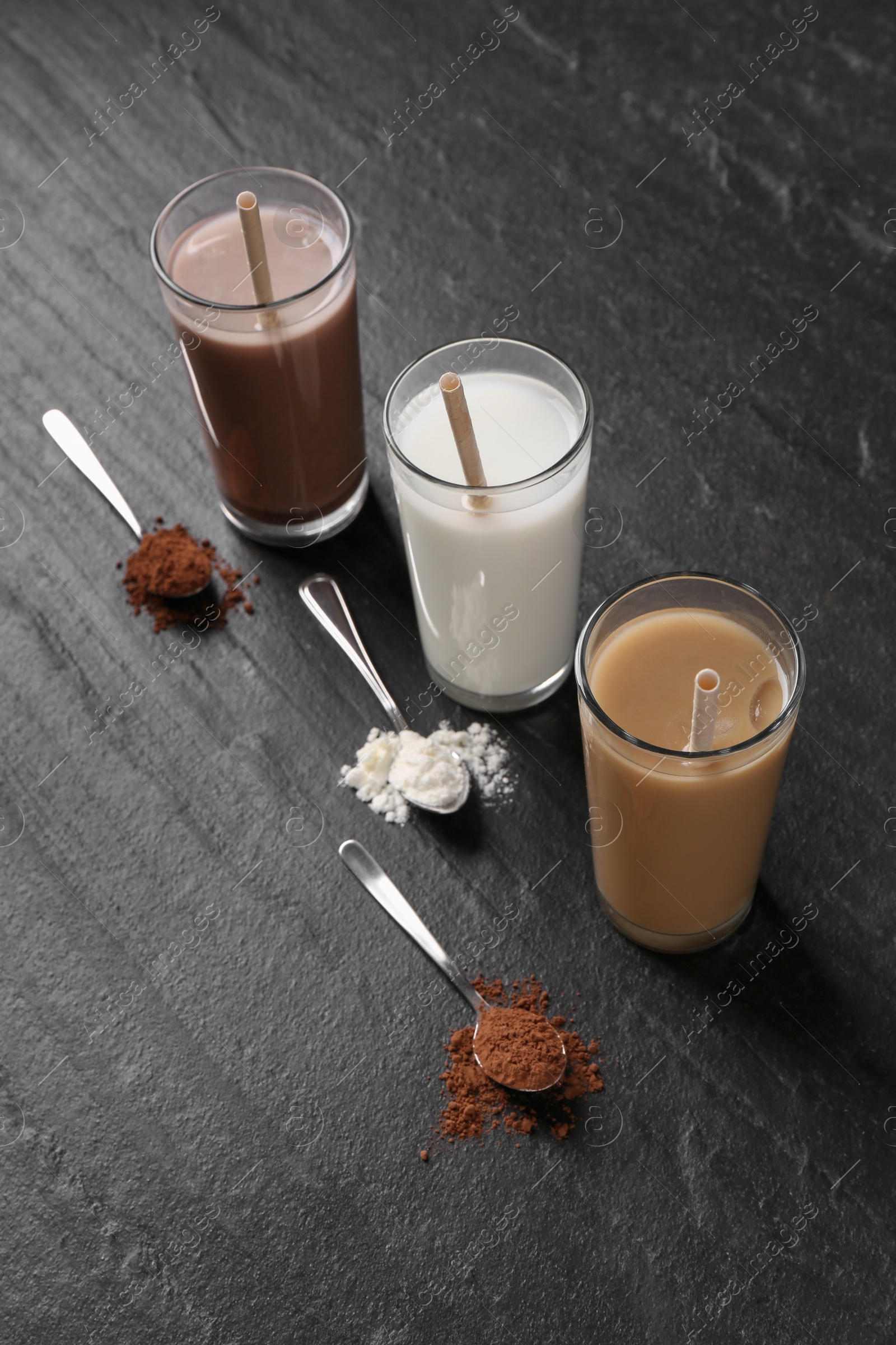 Photo of Delicious protein shakes in glasses and spoons with powder on black table