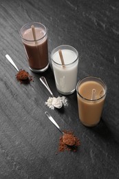 Photo of Delicious protein shakes in glasses and spoons with powder on black table