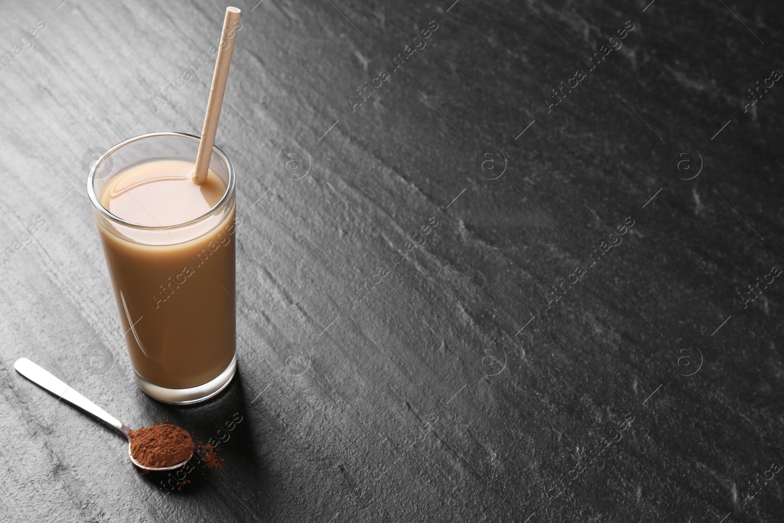 Photo of Delicious protein shake in glass and spoon with powder on black table, space for text