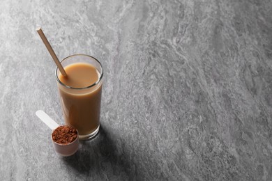 Photo of Delicious protein shake in glass and scoop with powder on grey table, space for text