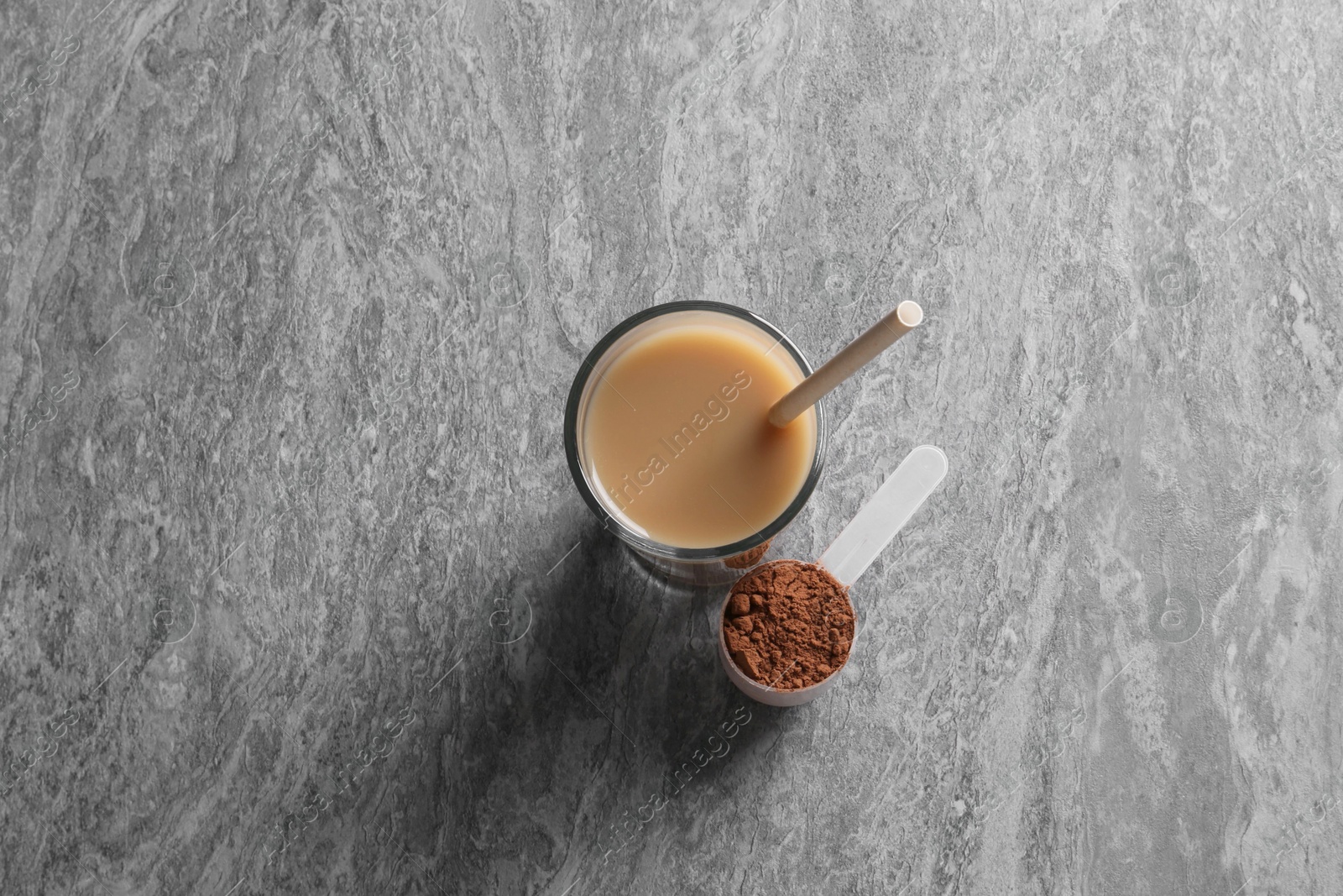 Photo of Delicious protein shake in glass and scoop with powder on grey table, top view