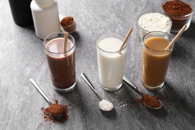 Photo of Delicious protein shakes in glasses, powder and spoons on grey table