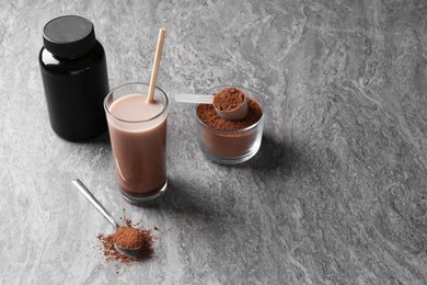 Photo of Delicious protein shake in glass, powder, spoon and plastic bottle on grey table, space for text