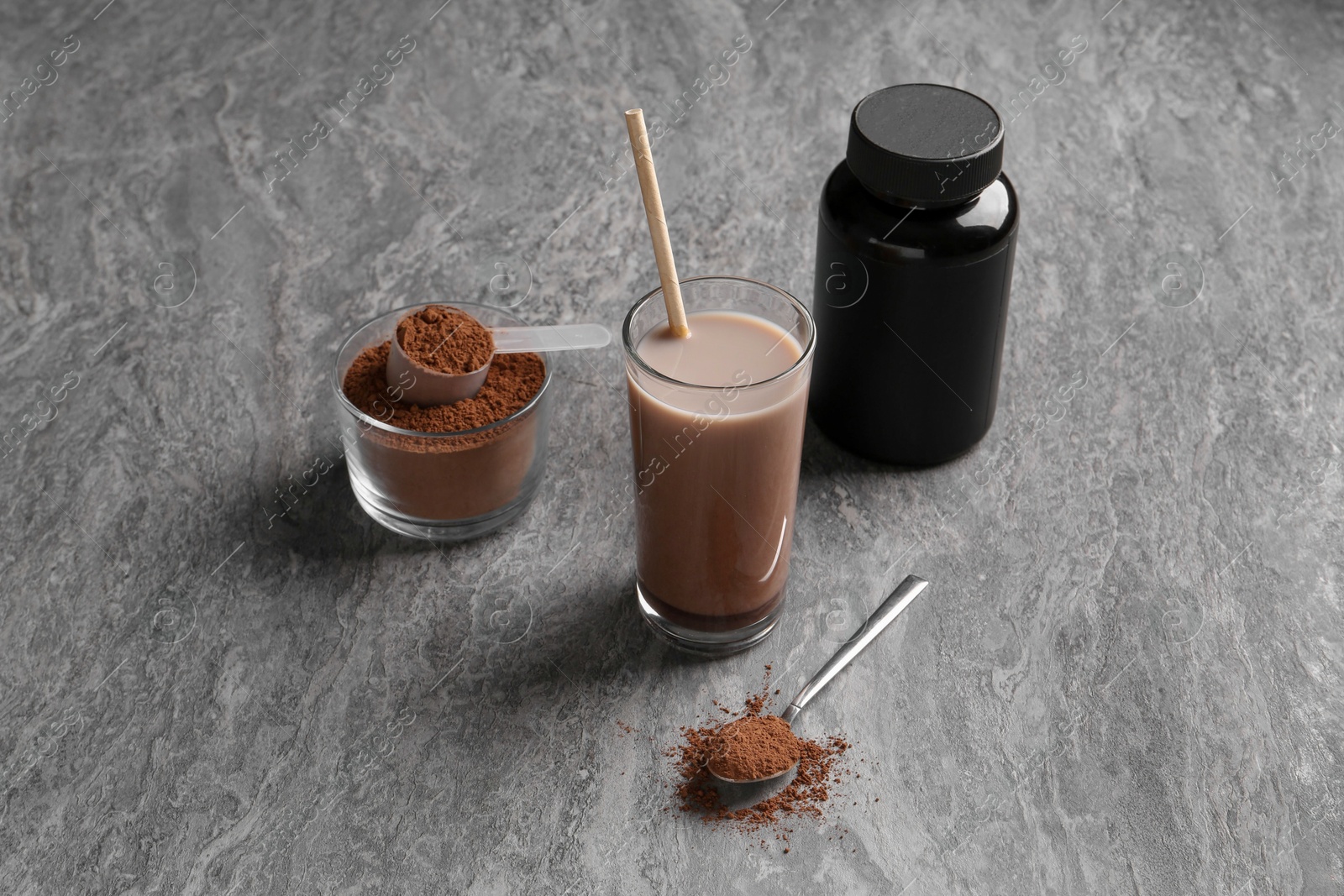 Photo of Delicious protein shake in glass, powder, spoon and plastic bottle on grey table