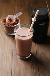 Photo of Delicious protein shake in glass, powder, scoop and plastic bottle on wooden table