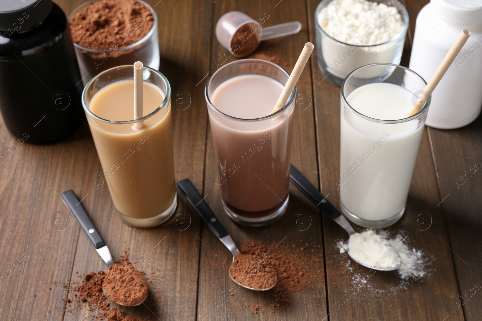 Photo of Delicious protein shakes in glasses, powder and spoons on wooden table