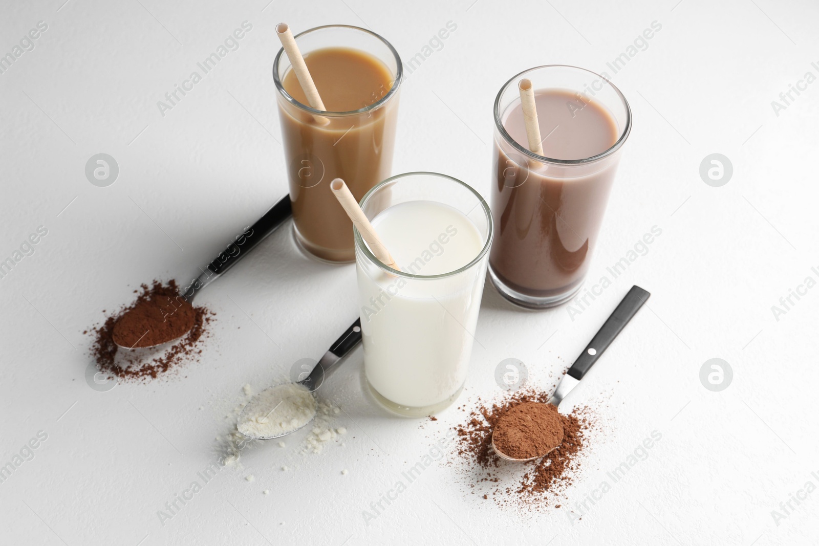 Photo of Delicious protein shakes in glasses and spoons with powder on white background