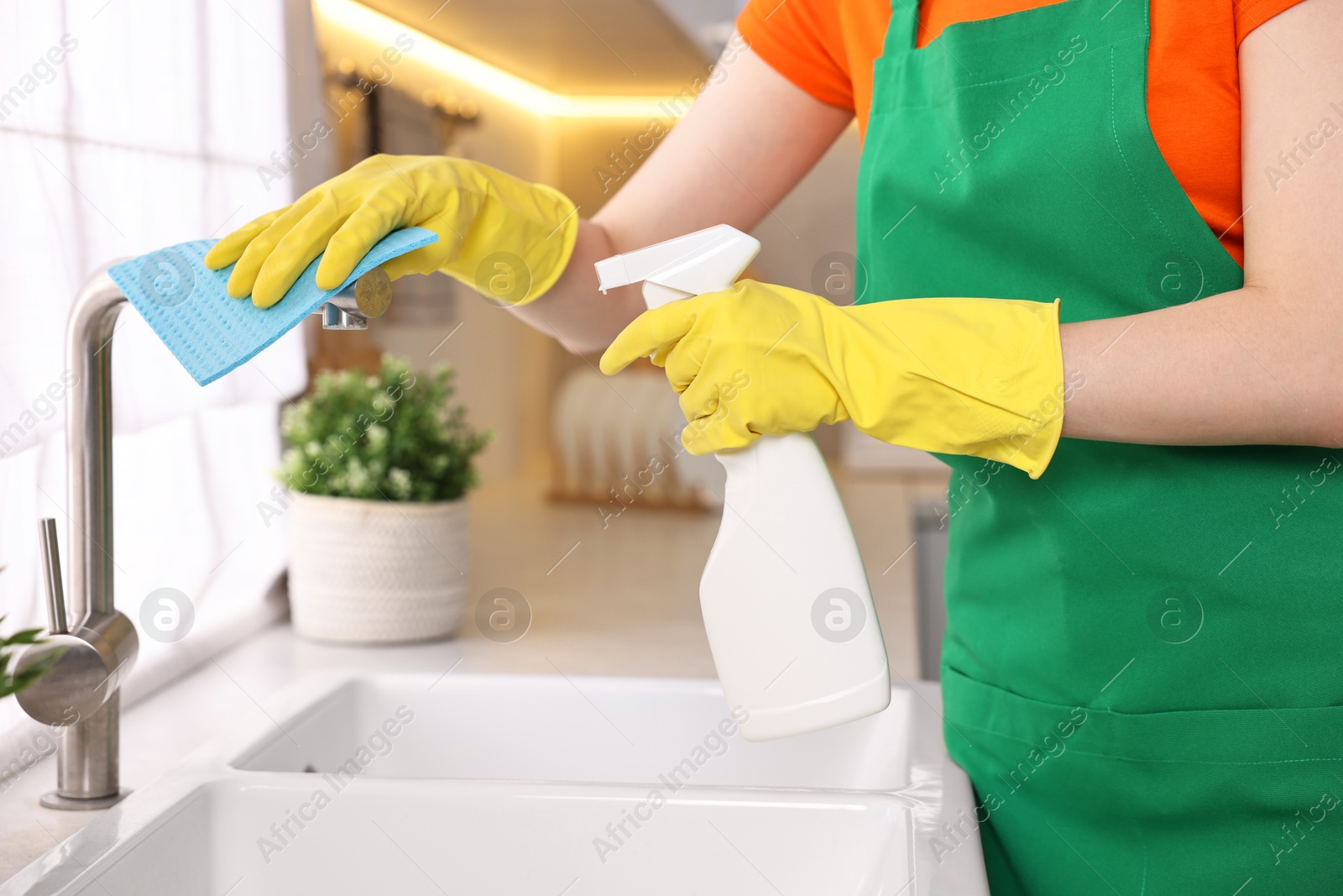 Photo of Professional janitor wearing uniform cleaning tap in kitchen, closeup