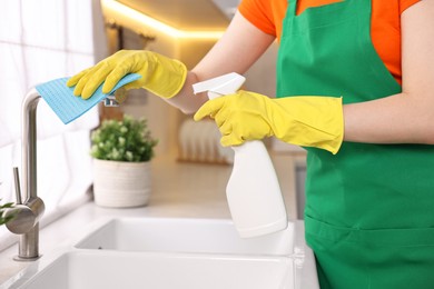 Professional janitor wearing uniform cleaning tap in kitchen, closeup