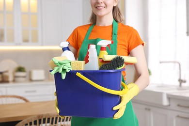 Photo of Cleaning service worker holding bucket with supplies in kitchen, closeup