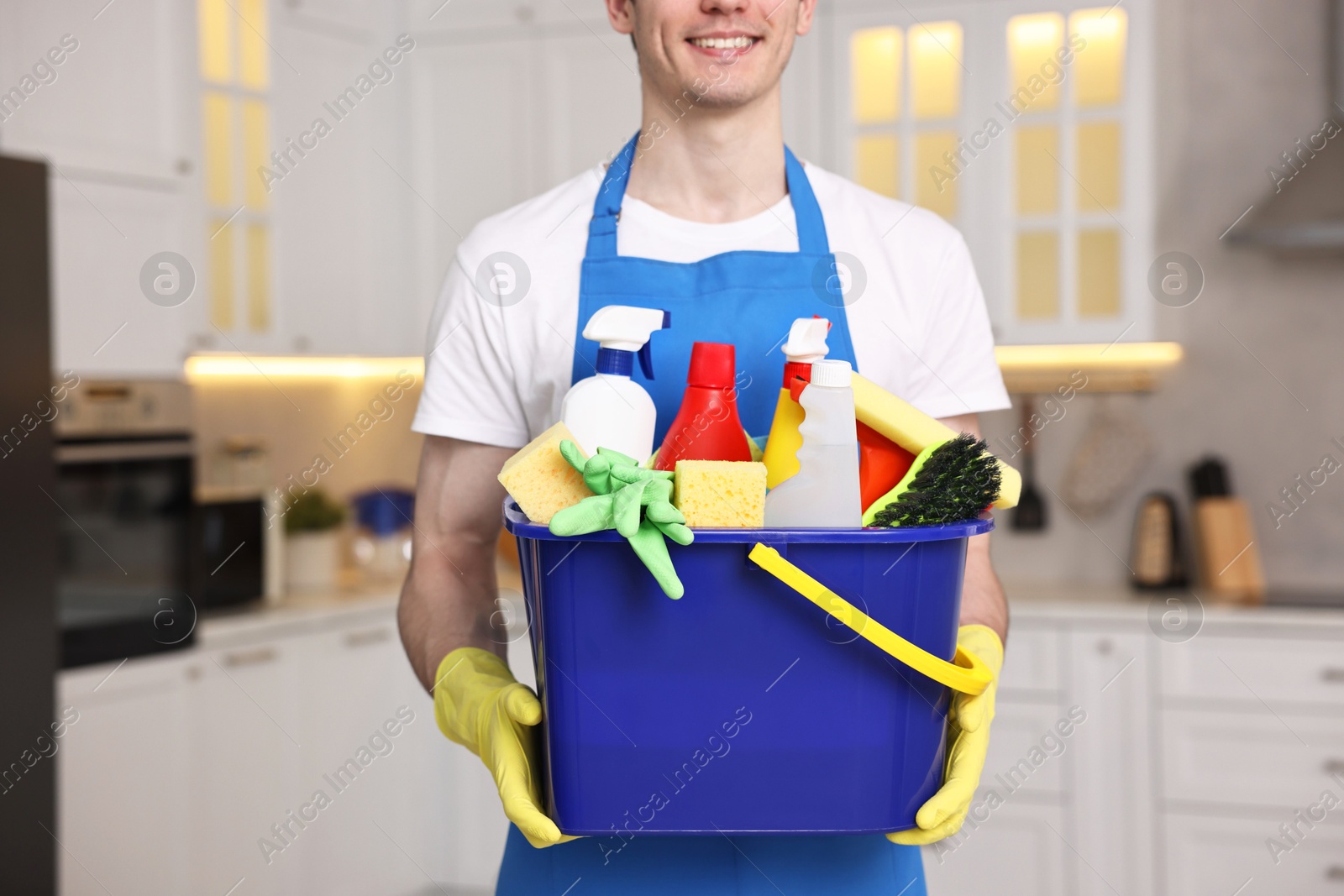 Photo of Cleaning service worker holding bucket with supplies in kitchen, closeup