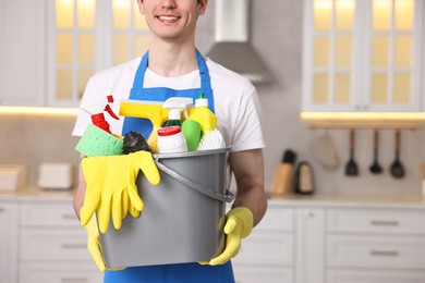 Photo of Cleaning service worker holding bucket with supplies in kitchen, closeup. Space for text