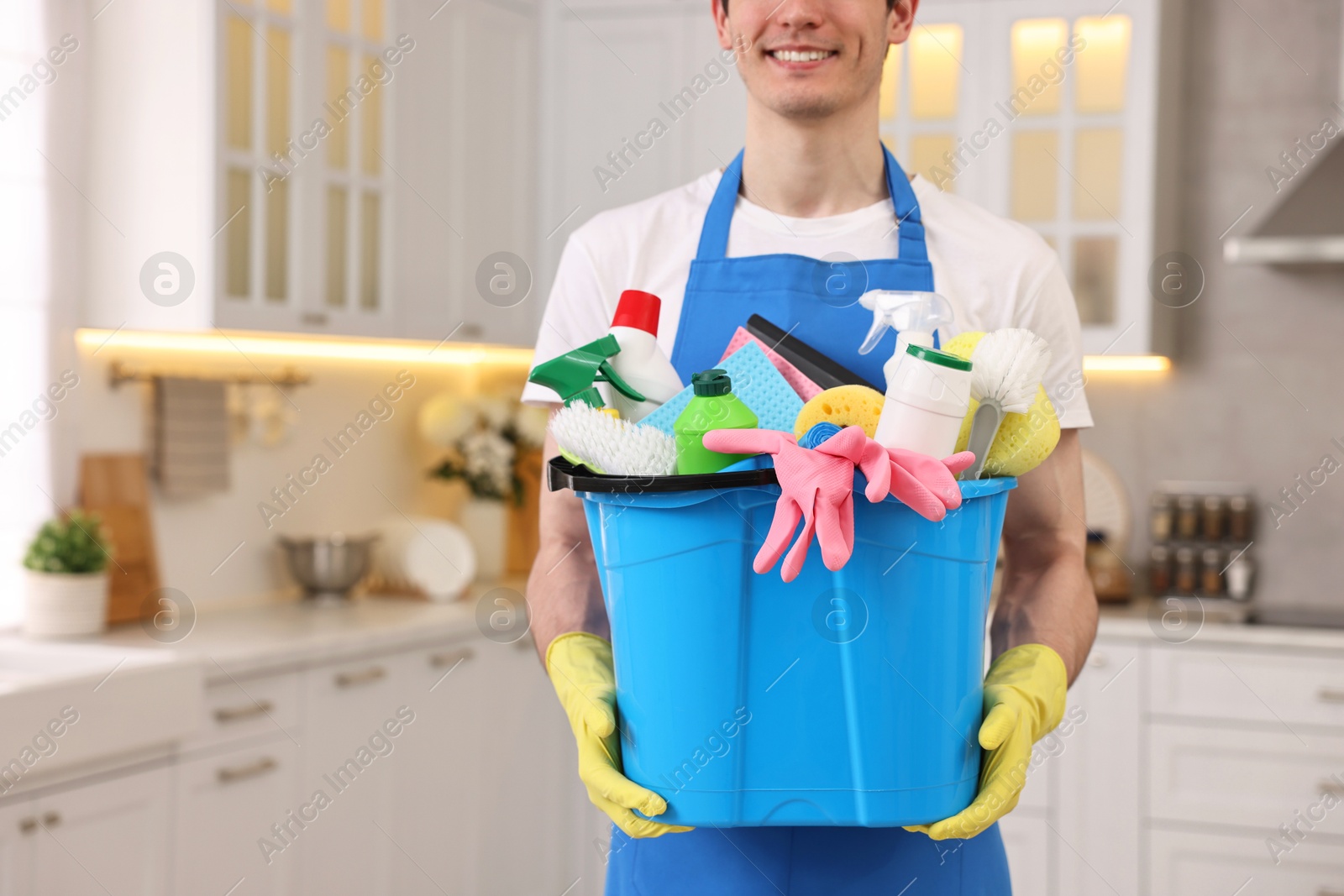 Photo of Cleaning service worker holding bucket with supplies in kitchen, closeup. Space for text