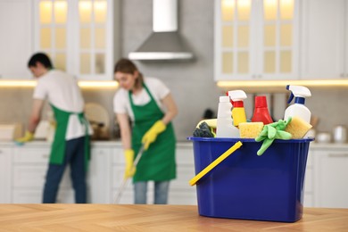 Photo of Professional janitors working in kitchen, focus on bucket with supplies. Cleaning service