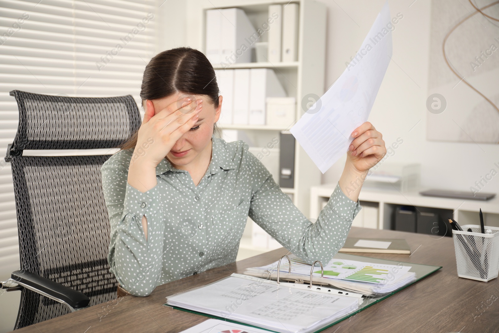 Photo of Embarrassed woman with document at wooden table in office