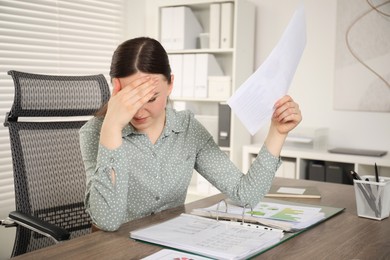 Embarrassed woman with document at wooden table in office