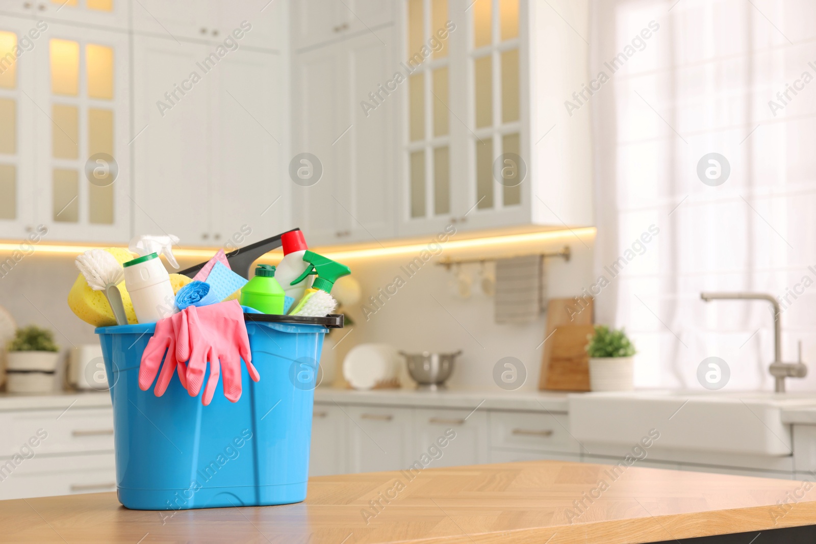 Photo of Cleaning service. Bucket with supplies on table in kitchen. Space for text