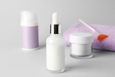 Photo of Bottle of chemical peel, cosmetic products, towel and brush on light background, closeup. Peeling procedure