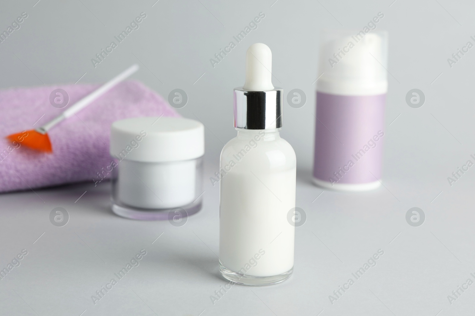 Photo of Bottle of chemical peel, cosmetic products, towel and brush on light background, closeup. Peeling procedure