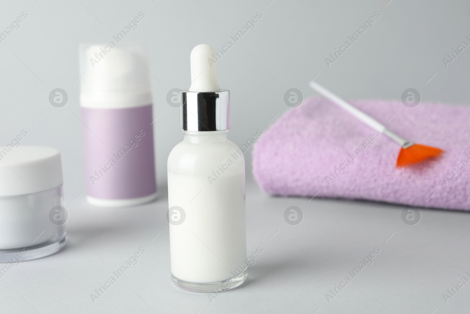 Photo of Bottle of chemical peel, cosmetic products, towel and brush on light background, closeup. Peeling procedure