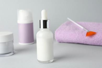 Bottle of chemical peel, cosmetic products, towel and brush on light background, closeup. Peeling procedure