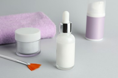 Photo of Bottle of chemical peel, cosmetic products, towel and brush on light background, closeup. Peeling procedure