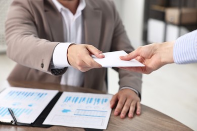 Boss giving salary in paper envelope to employee indoors, closeup