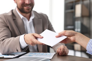 Boss giving salary in paper envelope to employee indoors, closeup