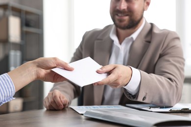 Boss giving salary in paper envelope to employee indoors, closeup