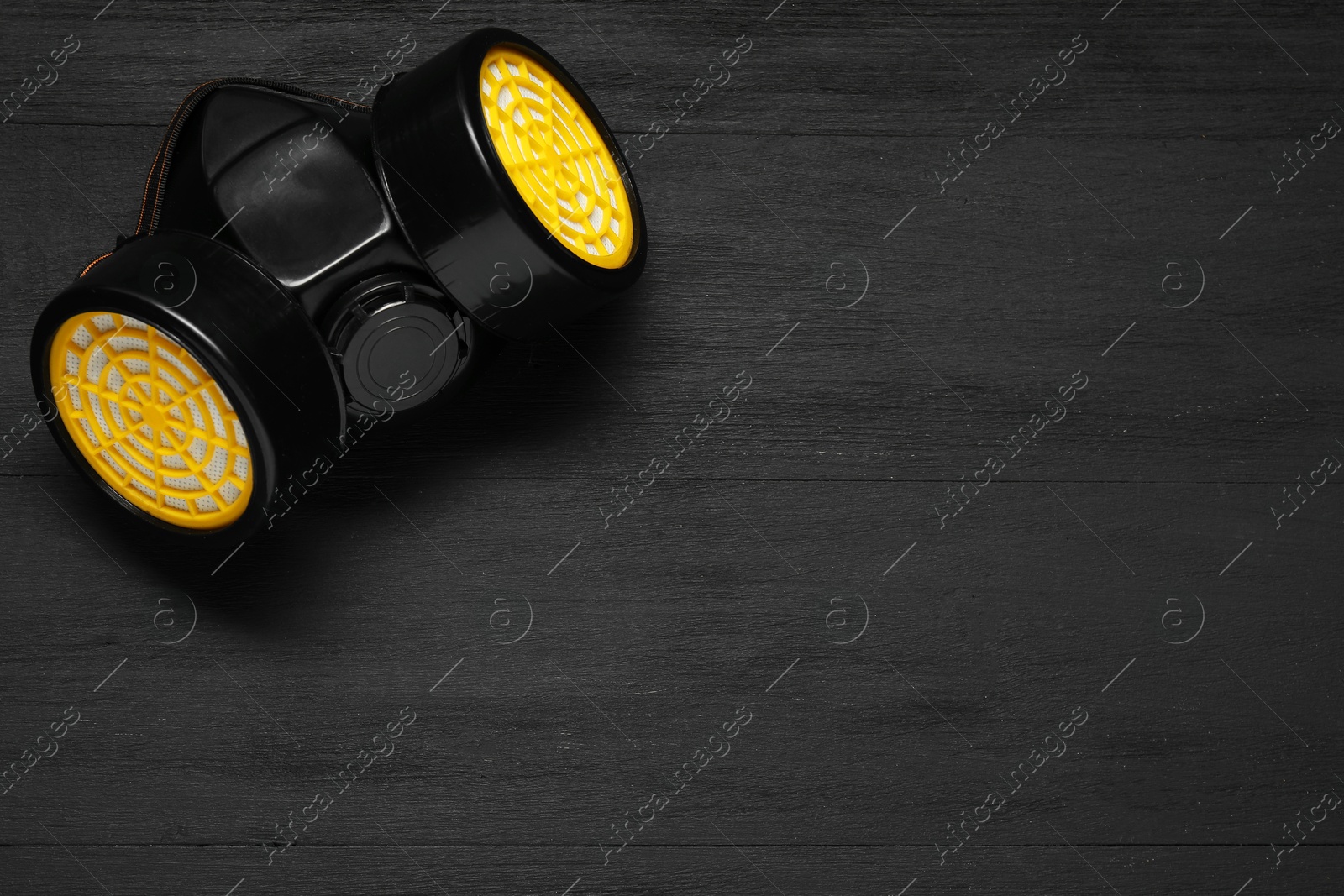 Photo of One respirator mask on black wooden background, top view. Space for text