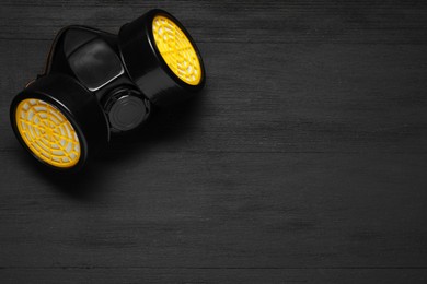 Photo of One respirator mask on black wooden background, top view. Space for text