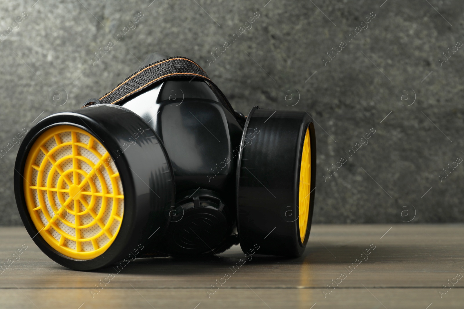 Photo of One respirator mask on wooden table against gray textured wall, space for text