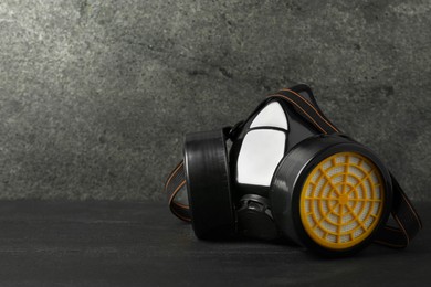 Photo of One respirator mask on black wooden table against gray textured wall, space for text