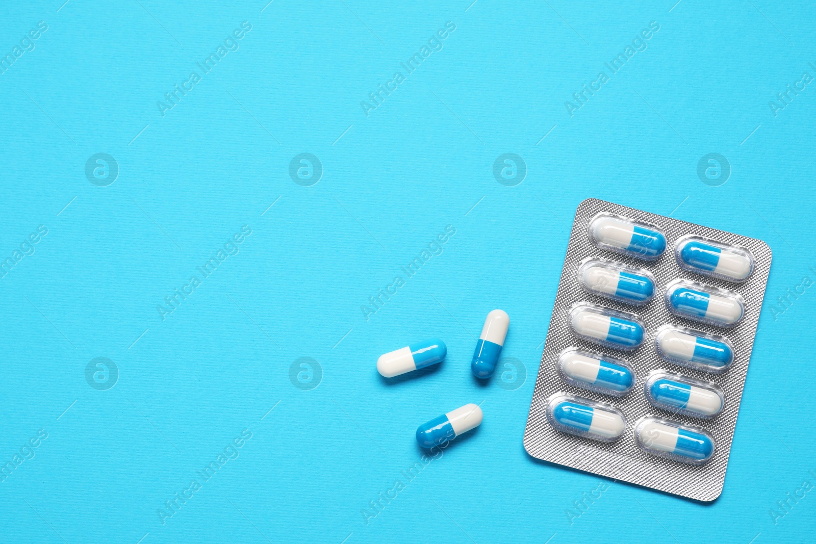 Photo of Antibiotic pills in blister on light blue background, top view. Space for text