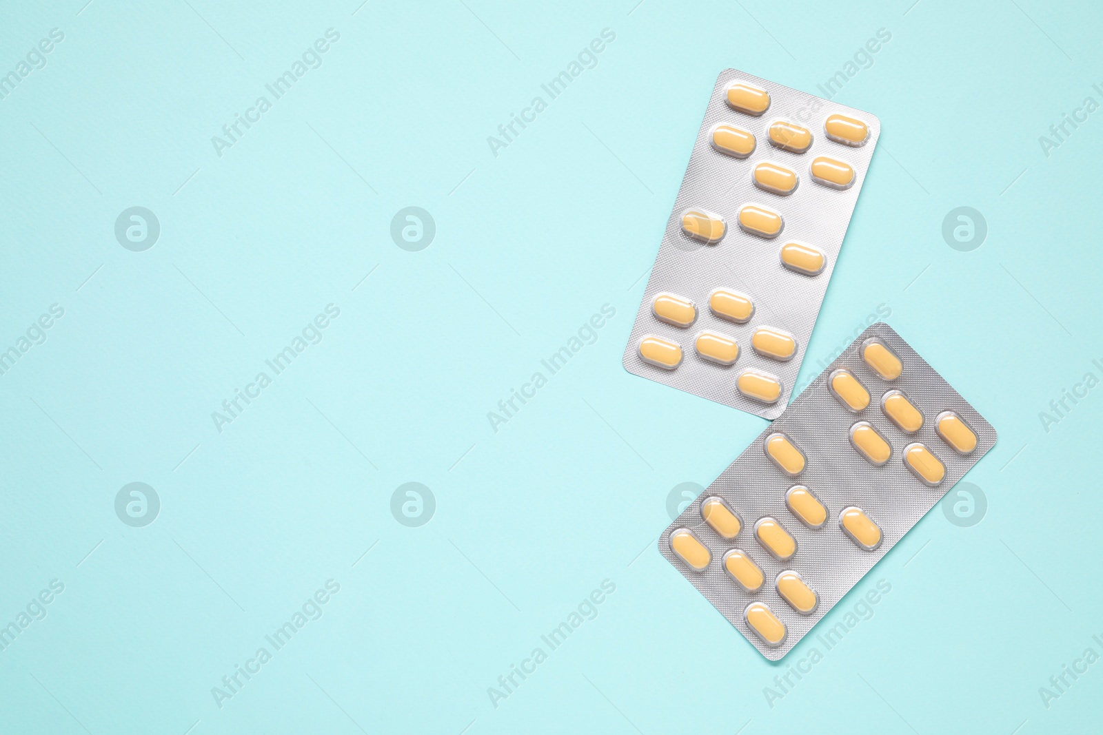 Photo of Antibiotic pills in blisters on light blue background, flat lay. Space for text