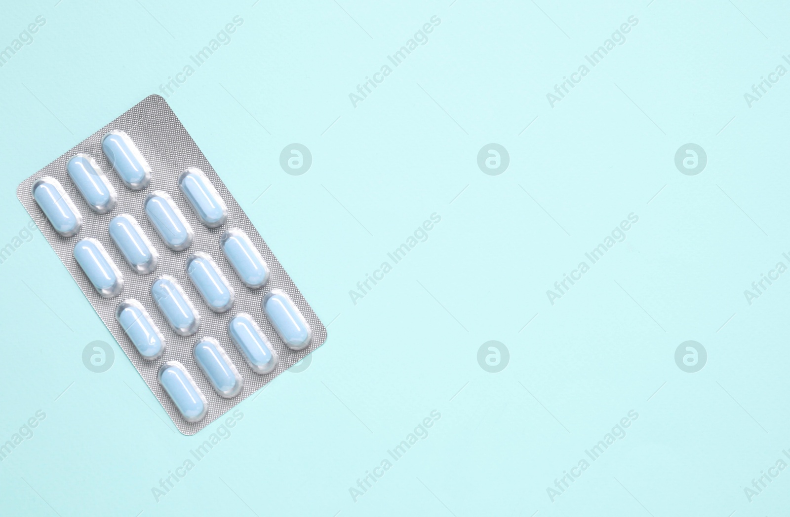 Photo of Antibiotic pills in blister on light blue background, top view. Space for text