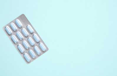 Photo of Antibiotic pills in blister on light blue background, top view. Space for text