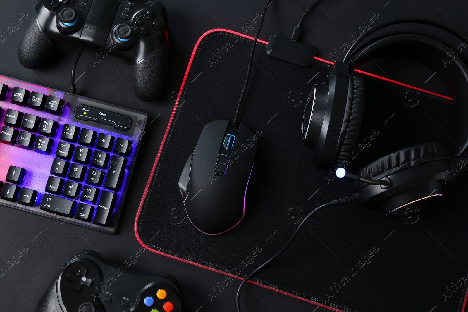 Photo of Computer mouse, RGB keyboard, game controllers and headset on black background, top view