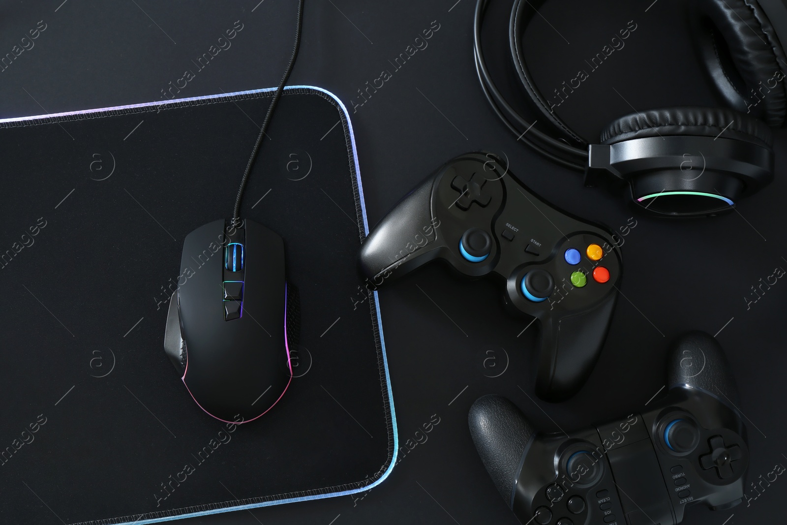 Photo of Computer mouse, mousepad, headset and game controllers on black background, flat lay