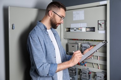 Photo of Technician worker with clipboard inspecting electricity meter indoors