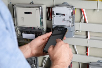 Technician worker with smartphone inspecting electricity meter, closeup